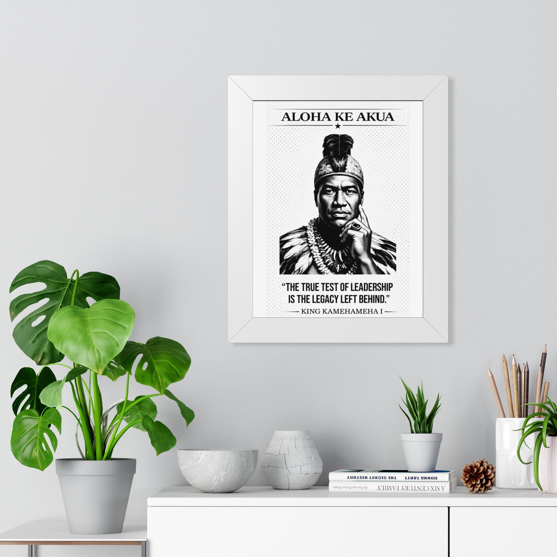 Framed ART with a portrait and quote on a wall above a white cabinet with decorative items.
