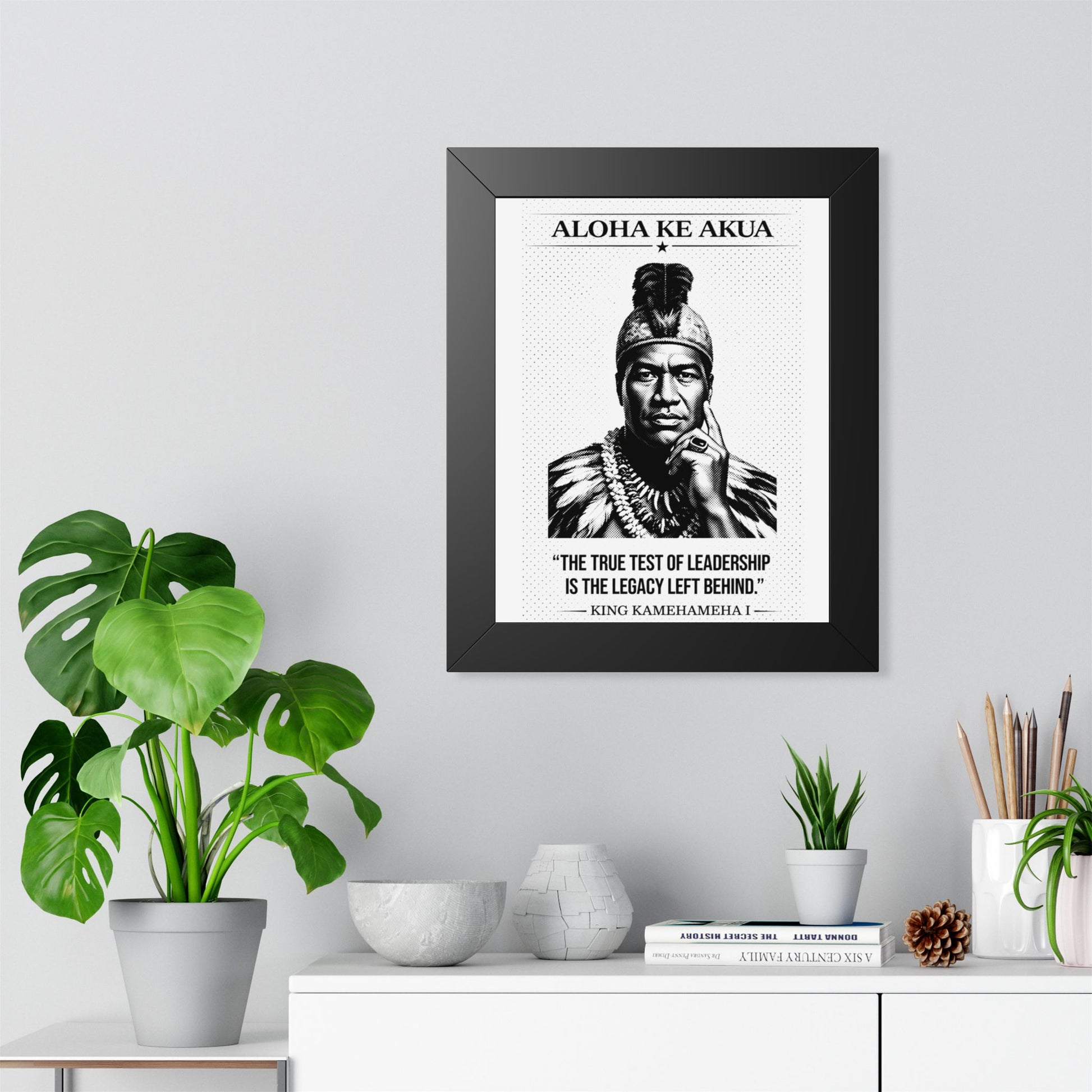Framed ART with a black and white portrait and text on a wall above a white cabinet with decorative items.