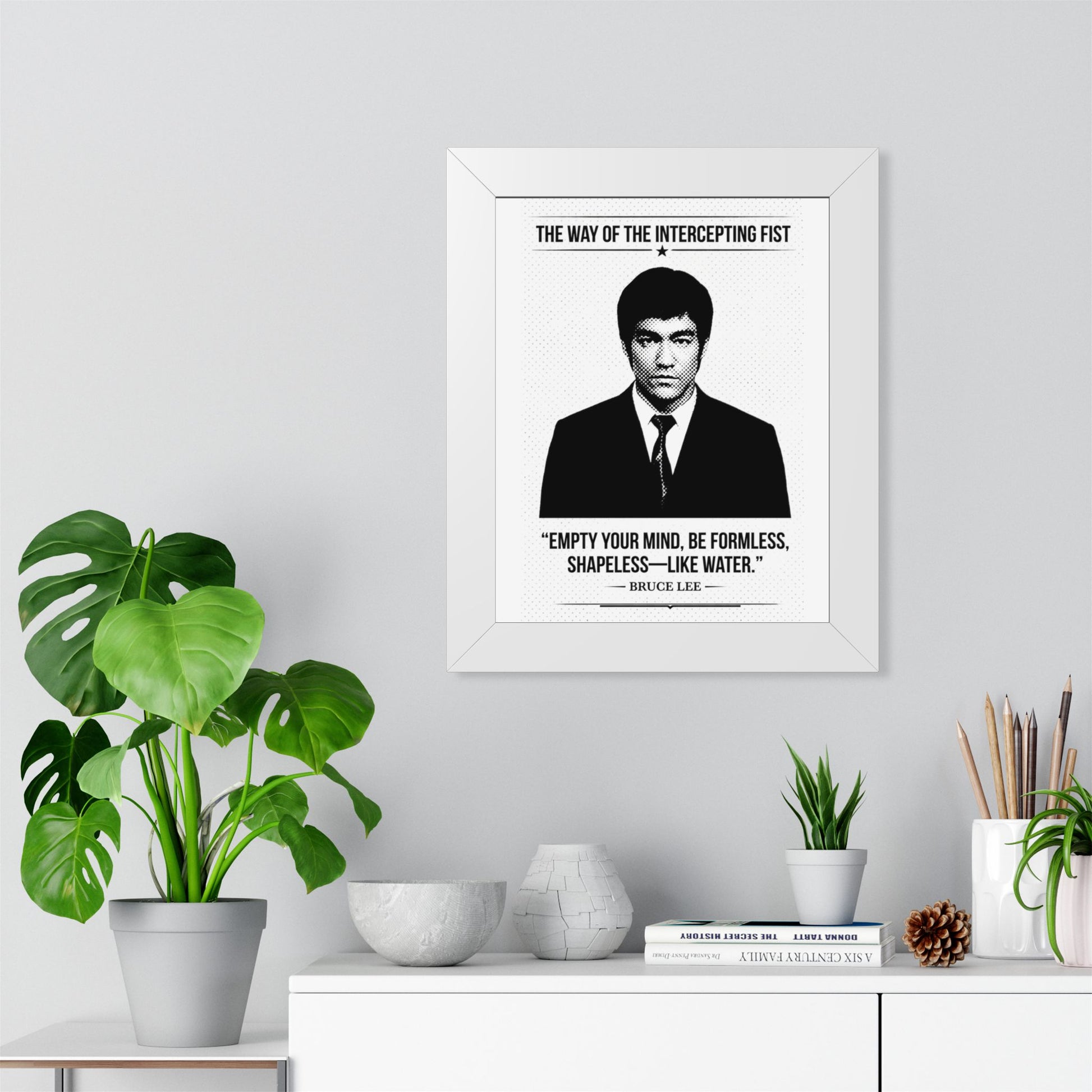 Framed Bruce Lee ART with a quote on a wall above a white cabinet with decorative items.