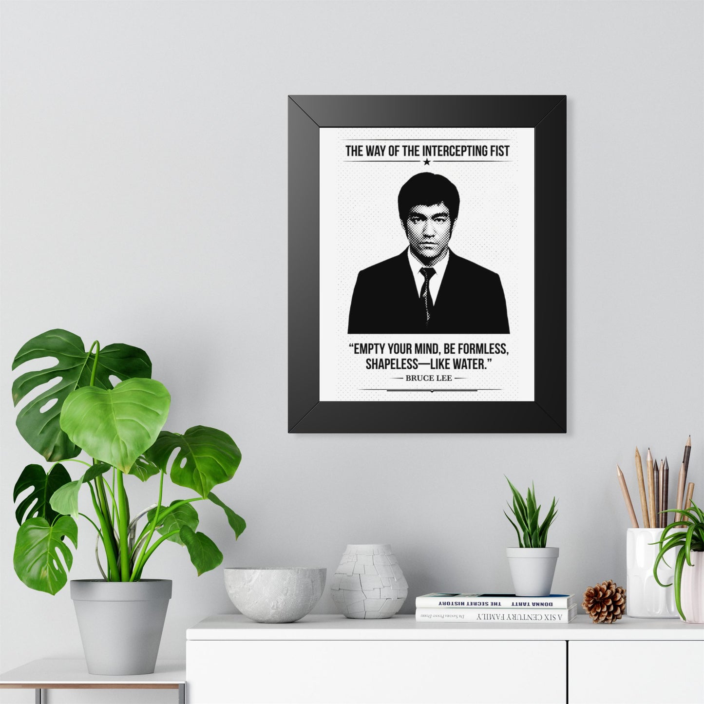 Framed Bruce Lee ART on a wall with decorative plants and items below.