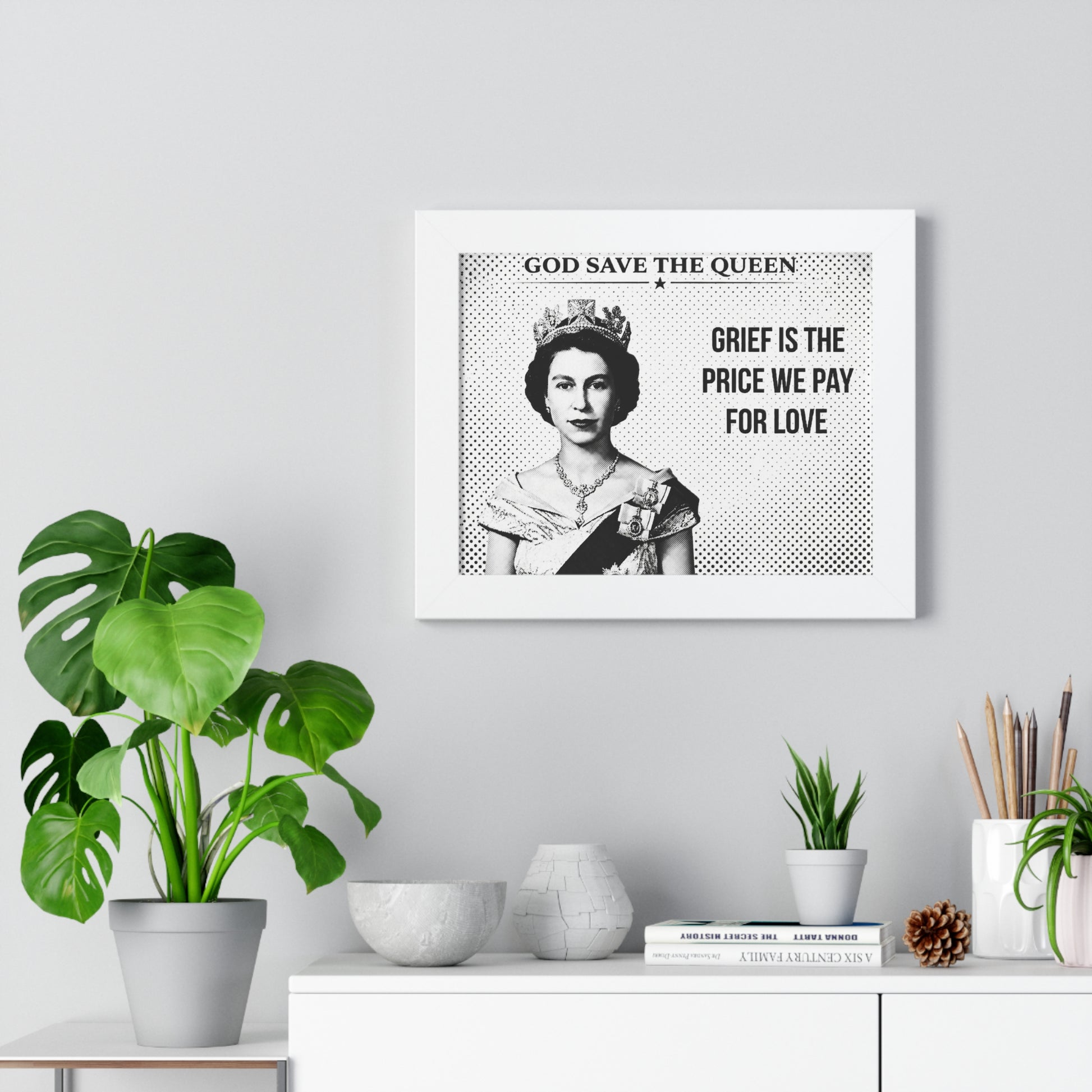 Framed artwork with a portrait of a queen and text on a wall with decor items below.