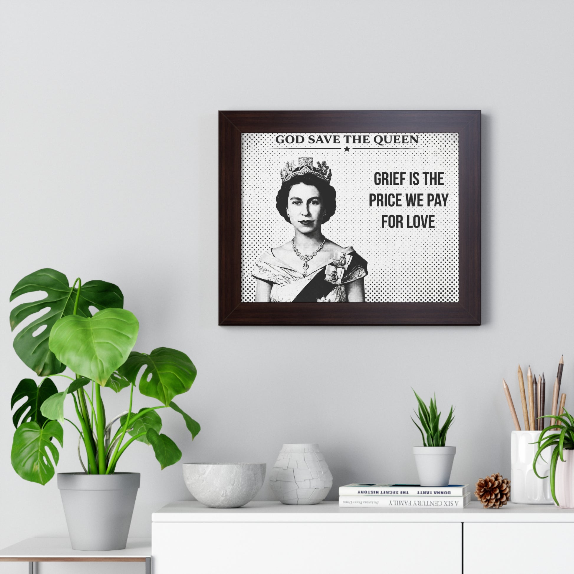 Framed portrait of a queen with text on a wall above a white cabinet with decorative items.