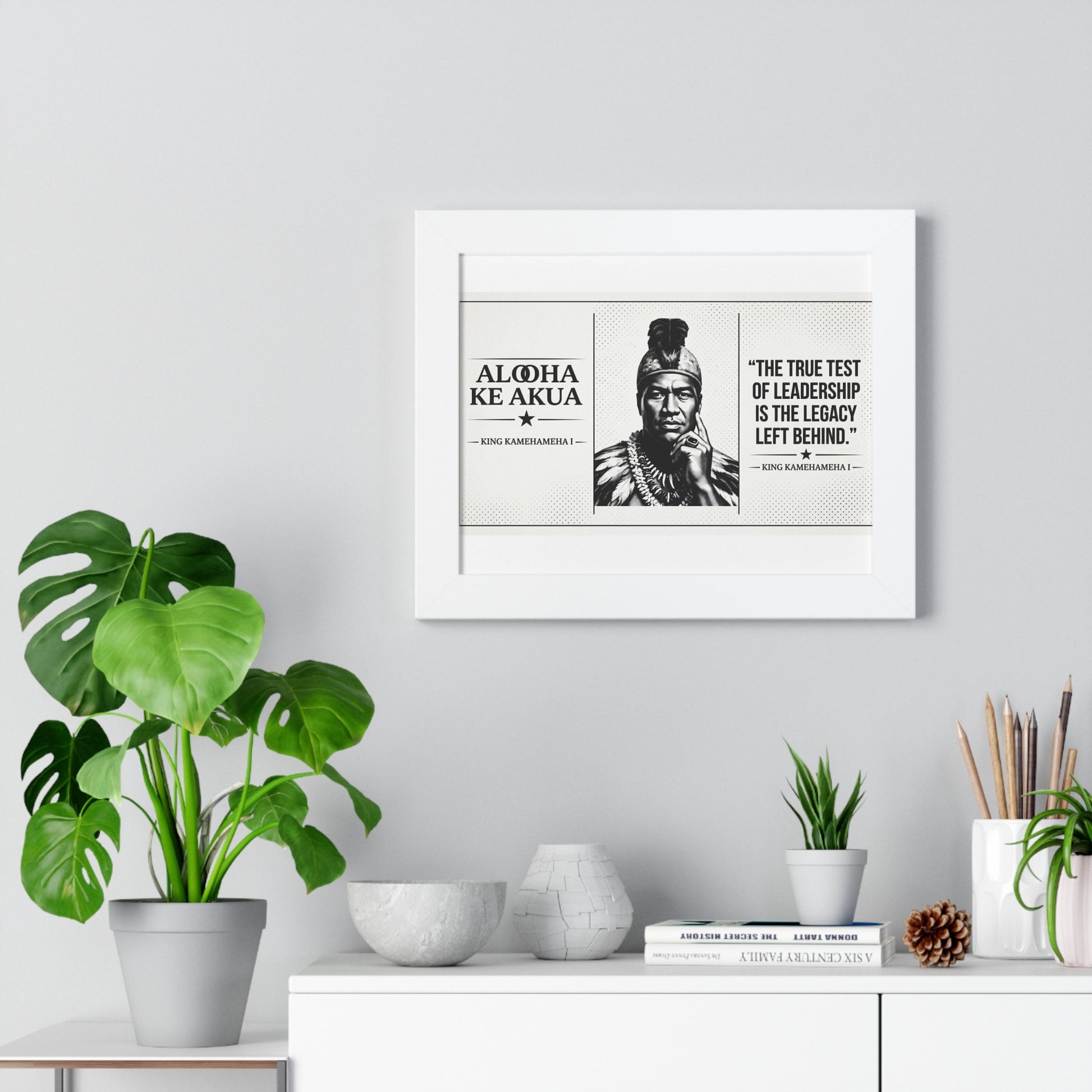 Framed artwork with a quote and portrait on a wall above a white cabinet with decorative items.