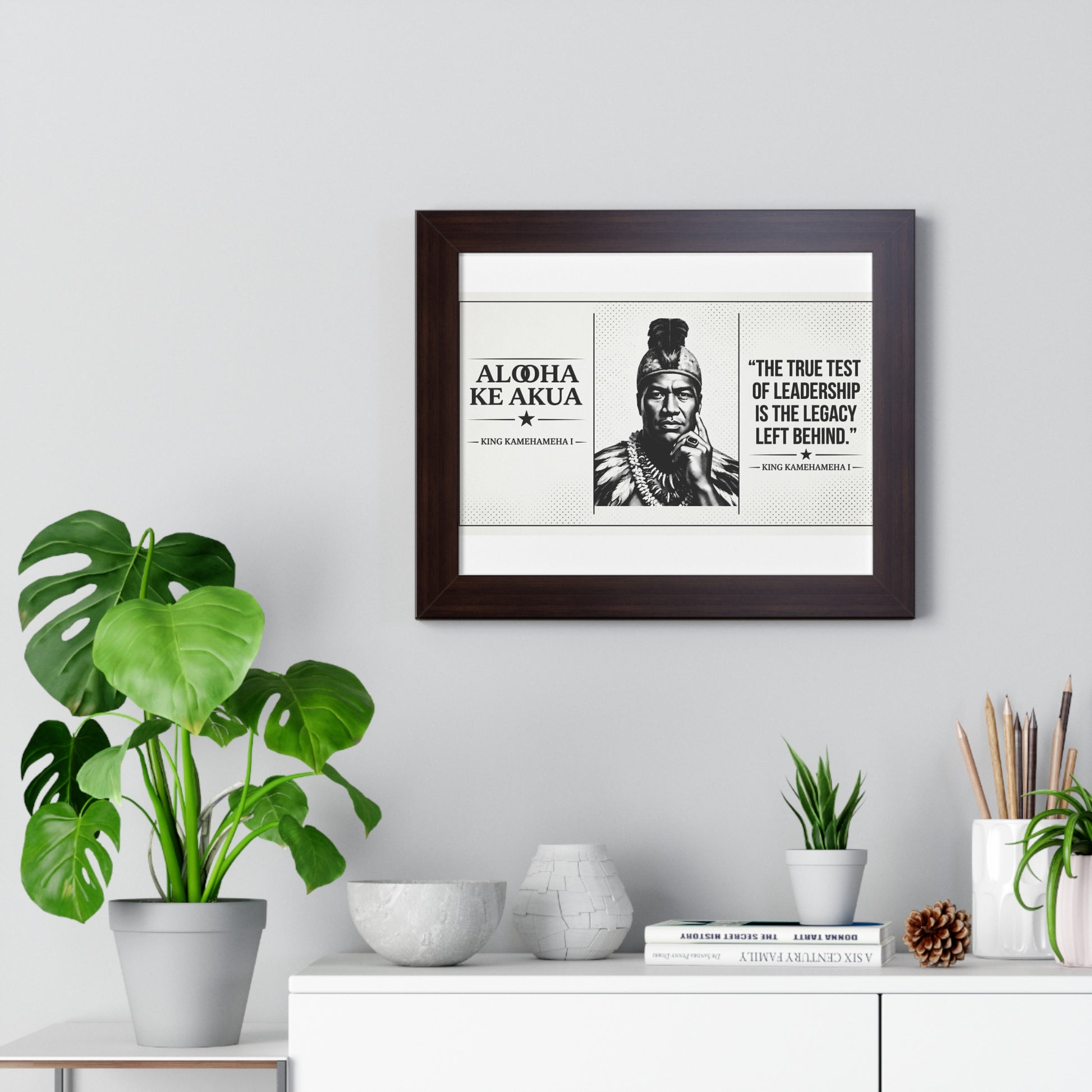 Framed print with a quote and portrait on a wall above a white cabinet with decorative items.