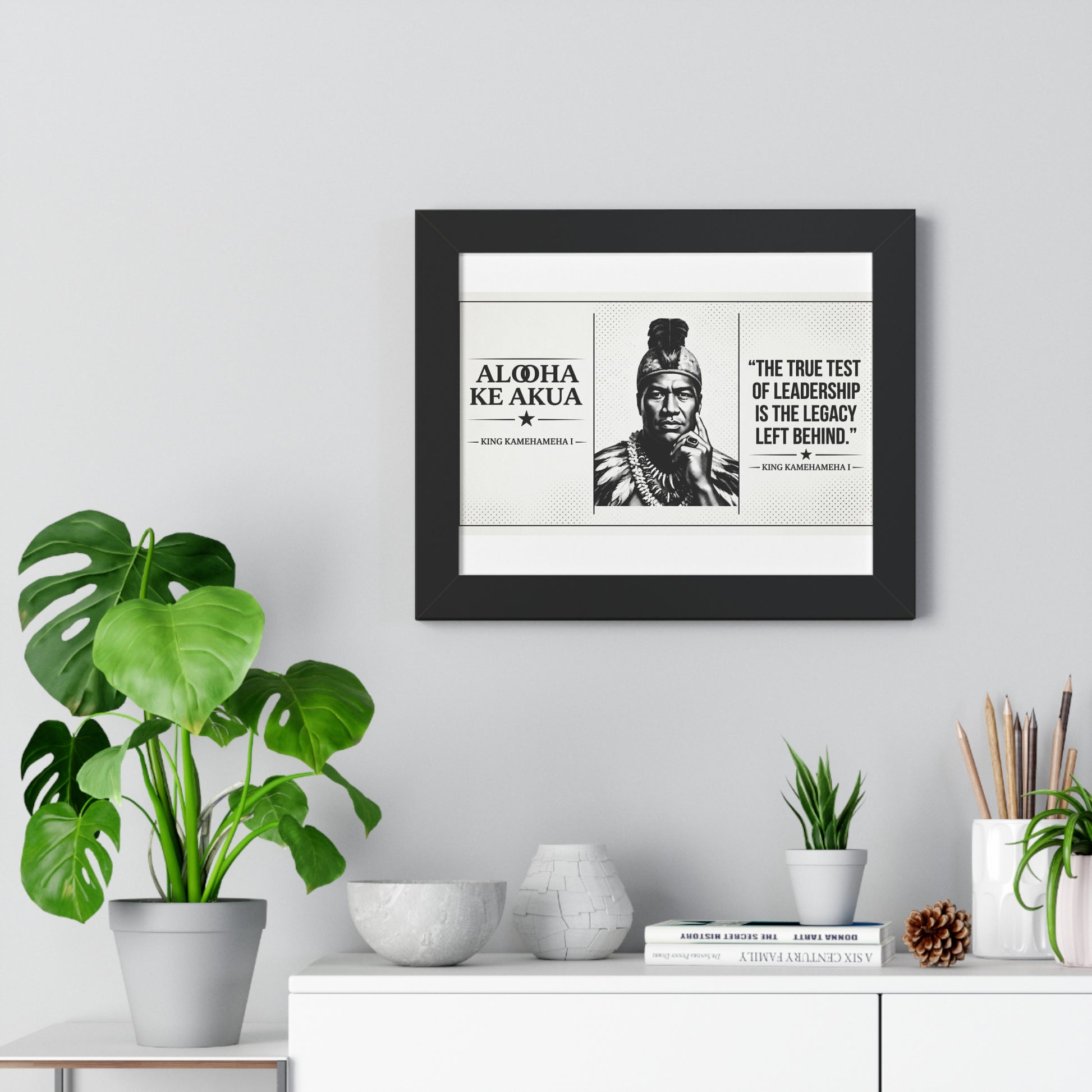 Framed print with a quote and portrait on a wall above a white cabinet with decorative items.