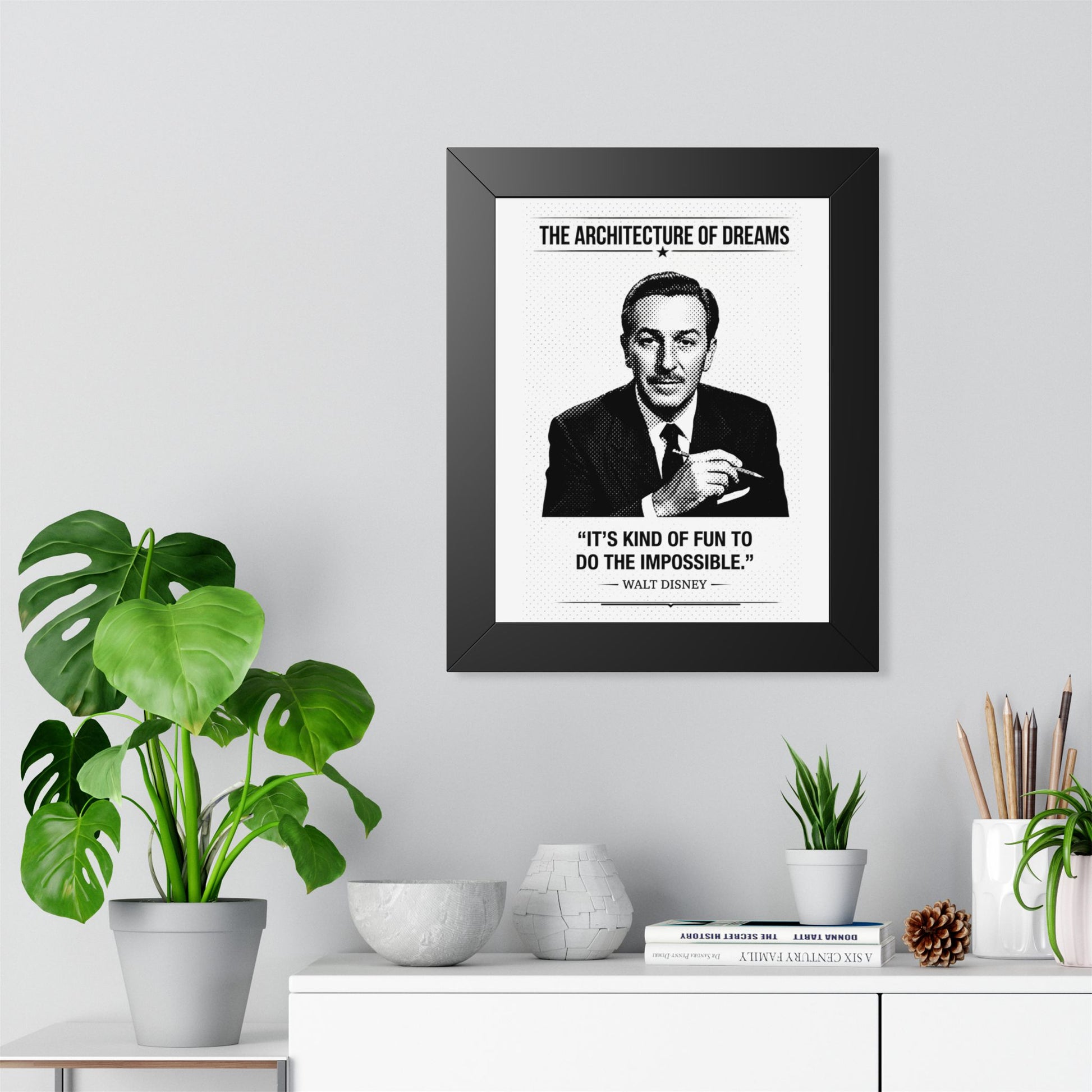 Framed ART with a black and white portrait of a man and motivational quote on a wall above a desk with plants.