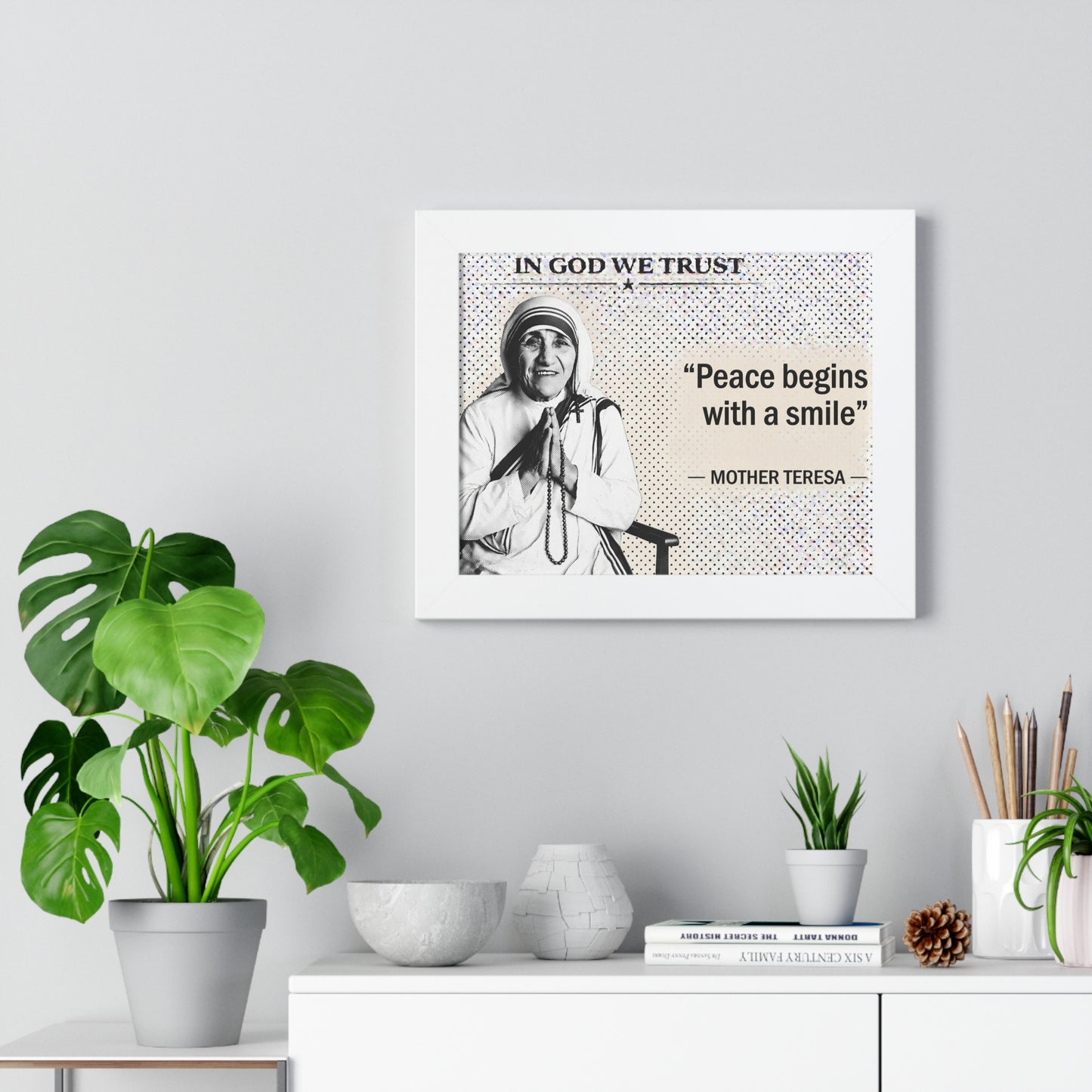 Framed Mother Teresa quote on a wall with decorative plants and items below.