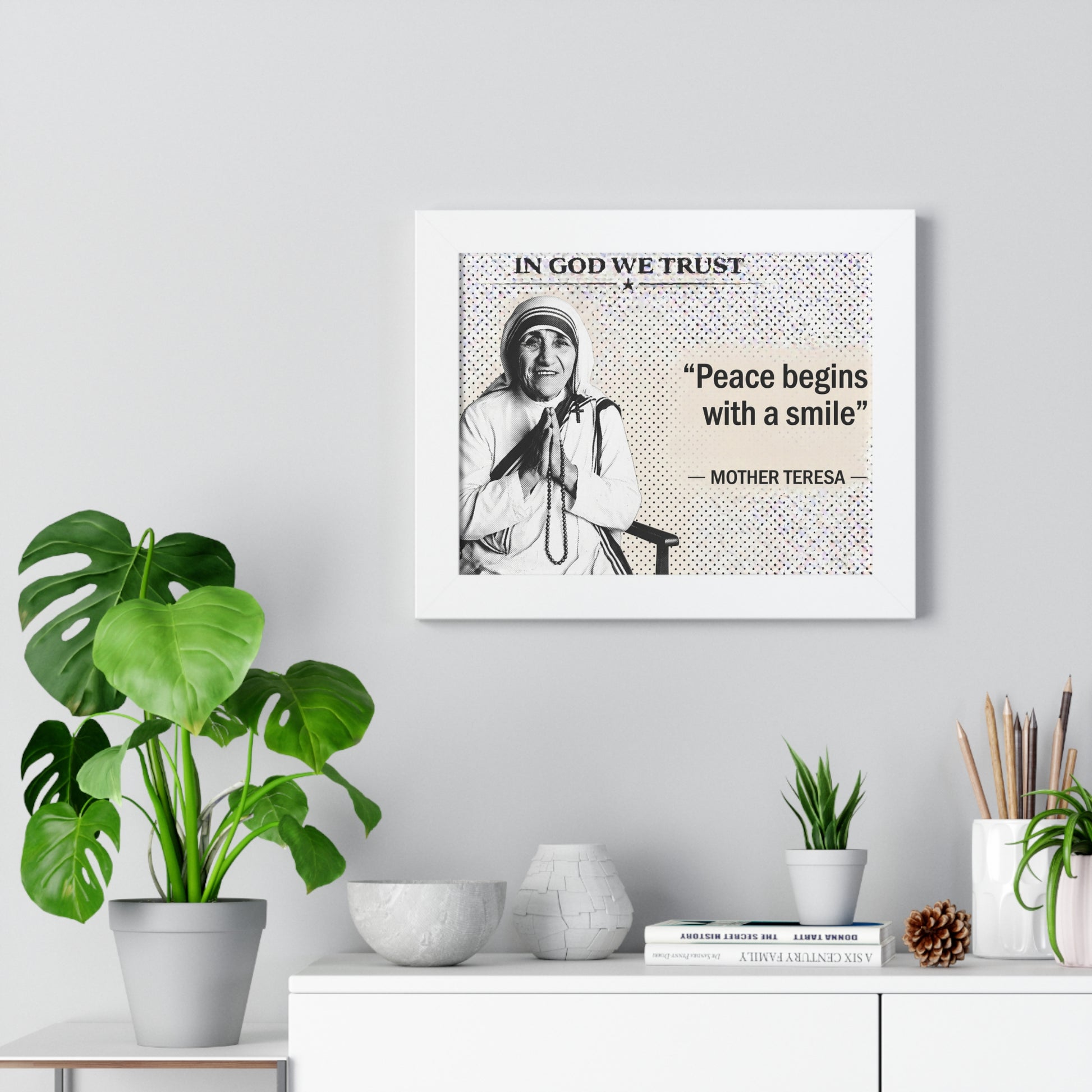 Framed Mother Teresa quote on a wall with decorative plants and items below.