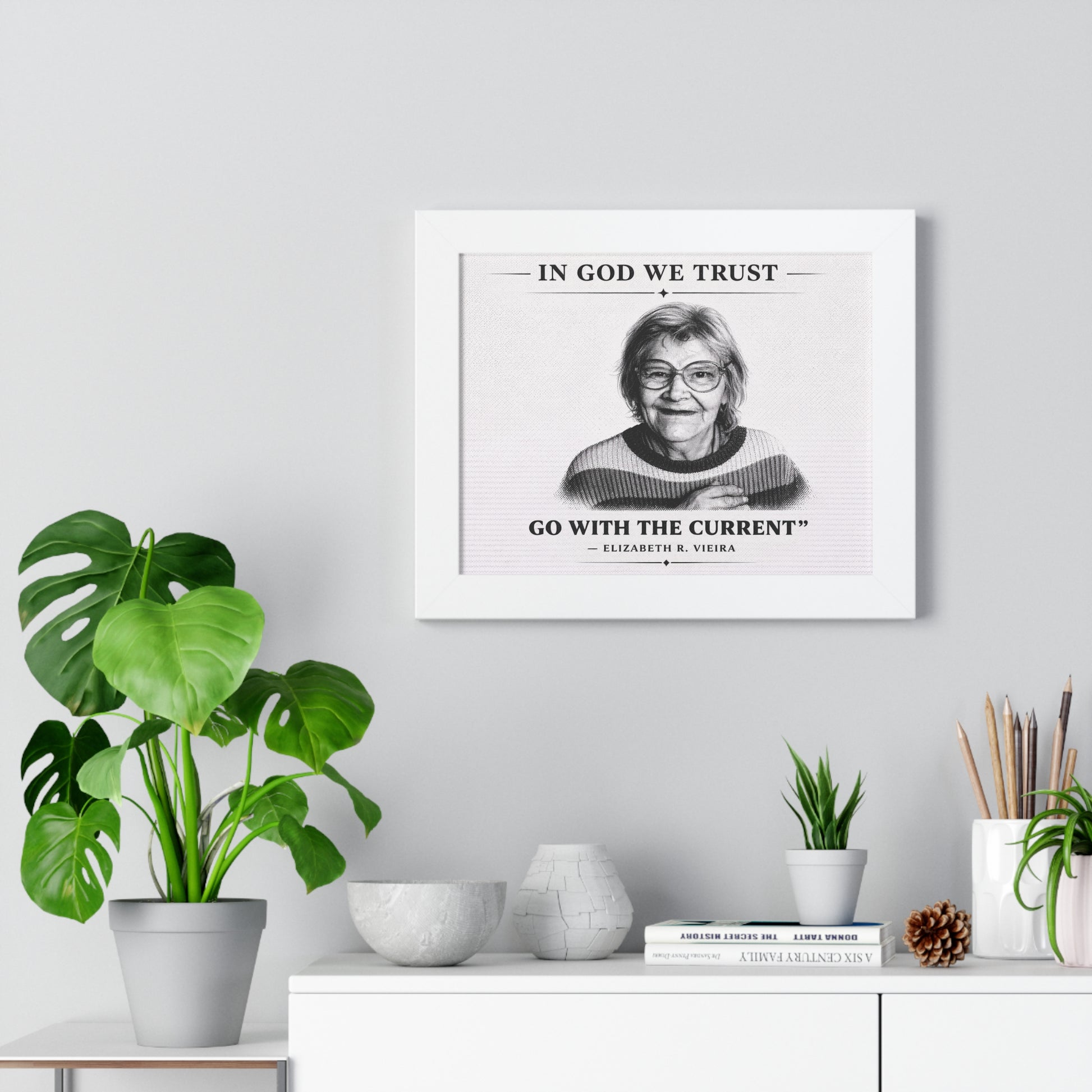 Framed portrait of a woman with a quote on a wall above a white cabinet with decorative items.