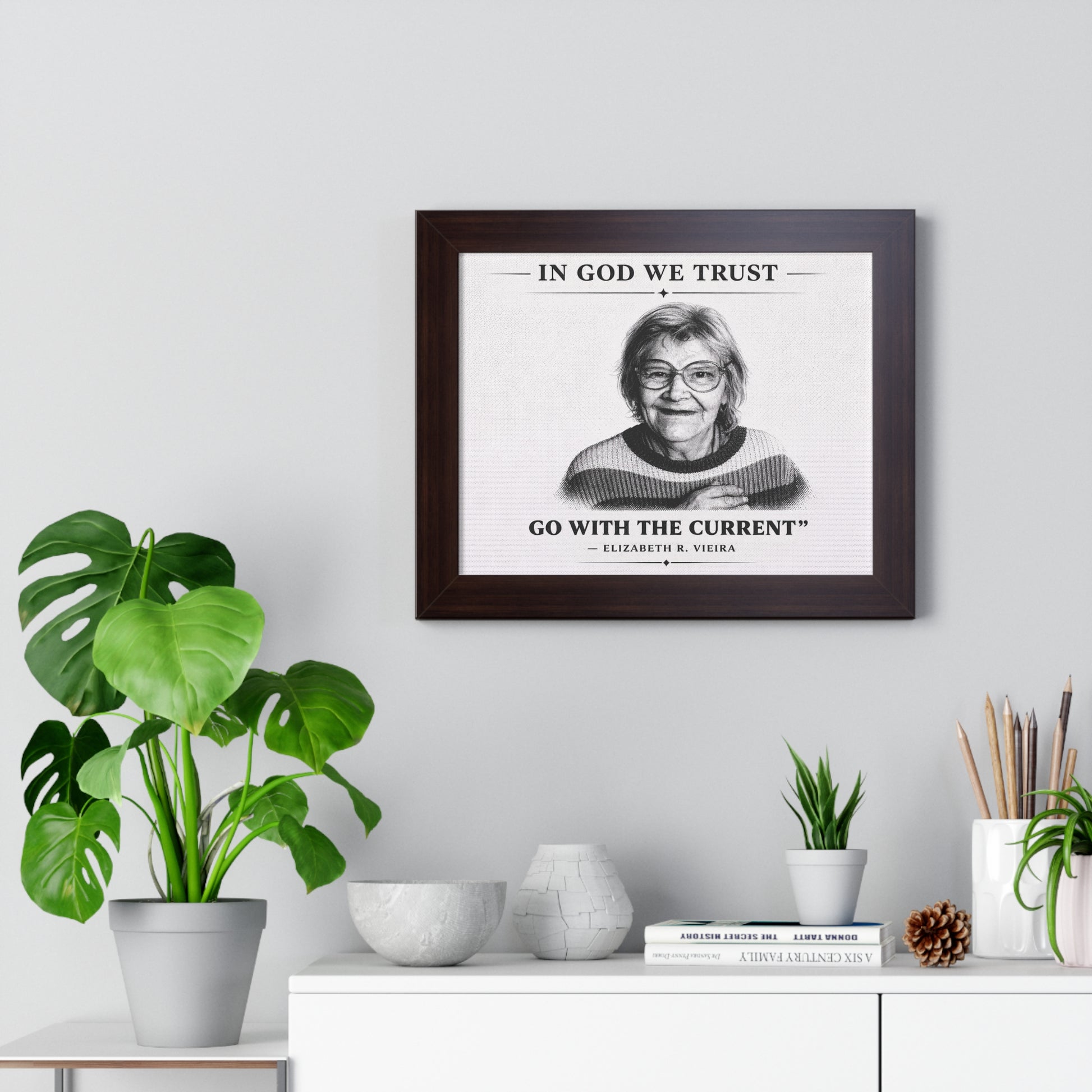 Framed print with a quote on a wall above a desk with plants and decor items.