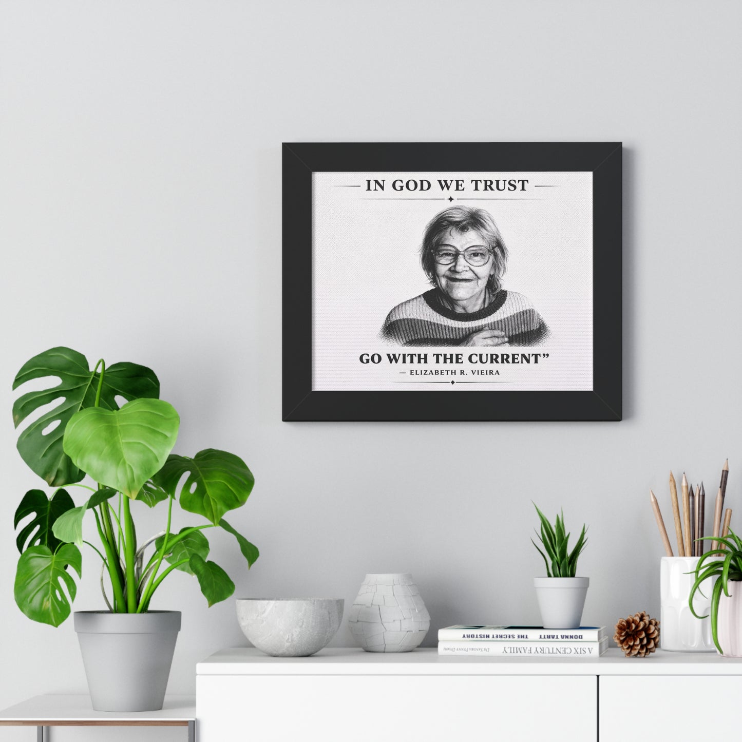 Framed print with a quote on a wall above a white cabinet with decorative items.